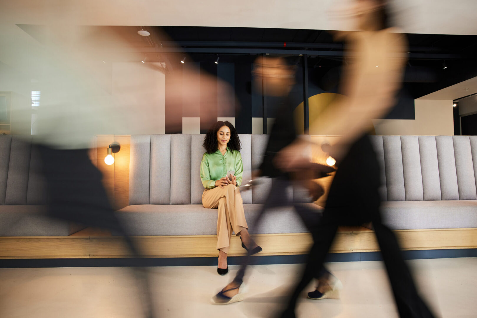 Smiling young businesswoman texting on her phone in an office lobby with blurred colleagues walking in the foreground